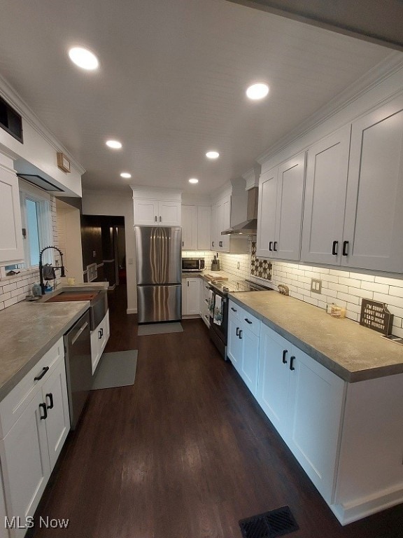 kitchen with appliances with stainless steel finishes, wall chimney exhaust hood, and white cabinetry