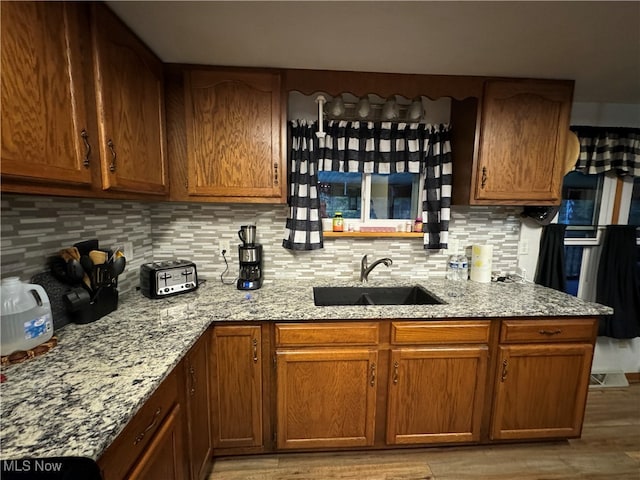 kitchen featuring backsplash, light stone counters, light hardwood / wood-style floors, and sink