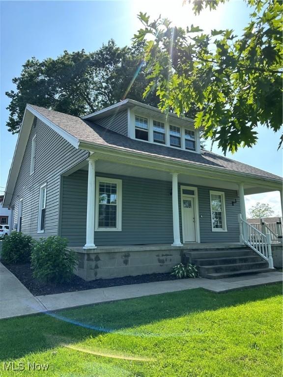 bungalow with a front lawn, a shingled roof, and covered porch