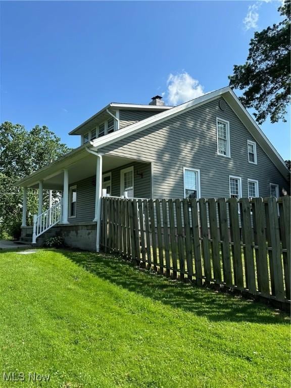 view of property exterior with a chimney, covered porch, fence, and a lawn