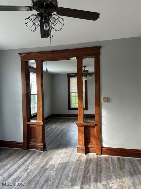 unfurnished living room featuring decorative columns, dark hardwood / wood-style flooring, and ceiling fan