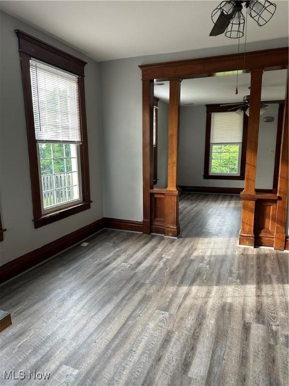 empty room with ceiling fan, decorative columns, wood finished floors, and baseboards