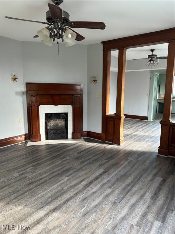 unfurnished living room with a tile fireplace, baseboards, a ceiling fan, and wood finished floors
