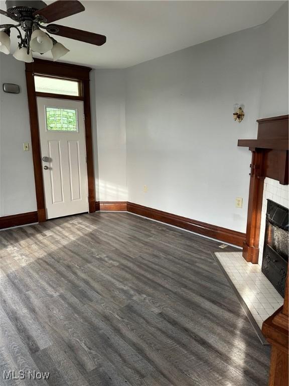 unfurnished living room featuring a tiled fireplace, baseboards, wood finished floors, and ceiling fan