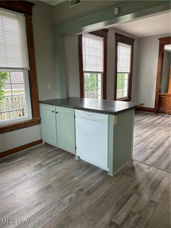 kitchen with a peninsula, wood finished floors, dark countertops, and white dishwasher