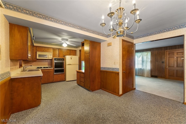 kitchen with ceiling fan with notable chandelier, light colored carpet, wooden walls, and white appliances