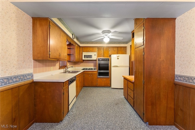 kitchen featuring white appliances, ceiling fan, wooden walls, sink, and light colored carpet