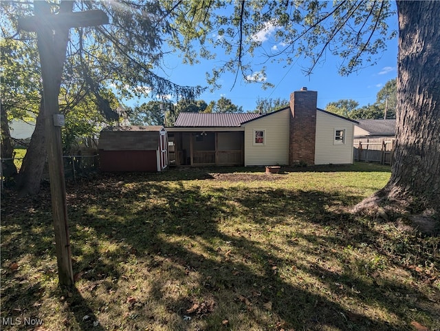 back of house featuring a sunroom, a lawn, and a storage unit