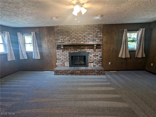 unfurnished living room featuring a textured ceiling, wooden walls, plenty of natural light, and a fireplace