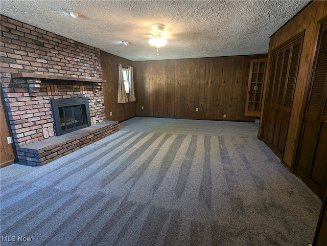 unfurnished living room featuring a textured ceiling, wooden walls, and carpet flooring