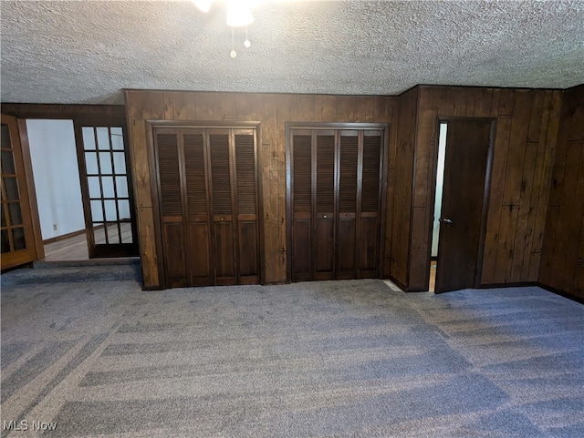 unfurnished bedroom with multiple closets, a textured ceiling, wood walls, and carpet floors