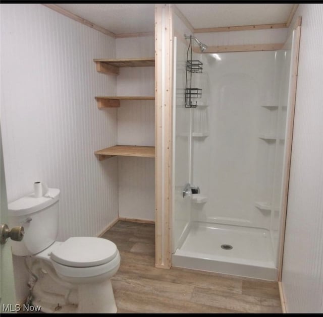 bathroom featuring a shower, toilet, crown molding, and hardwood / wood-style floors