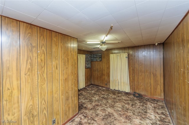 spare room featuring ceiling fan, wood walls, and carpet flooring