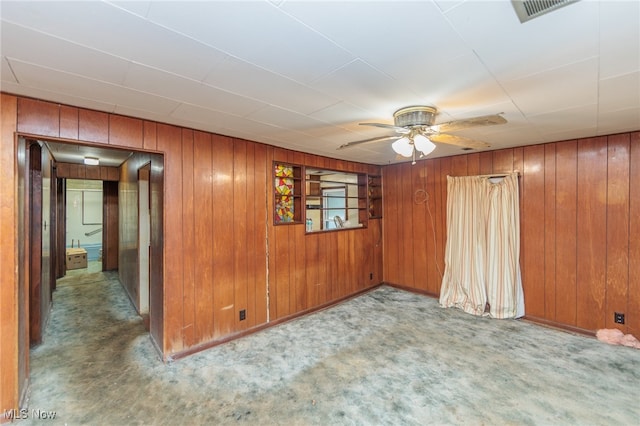 carpeted empty room featuring wooden walls and ceiling fan