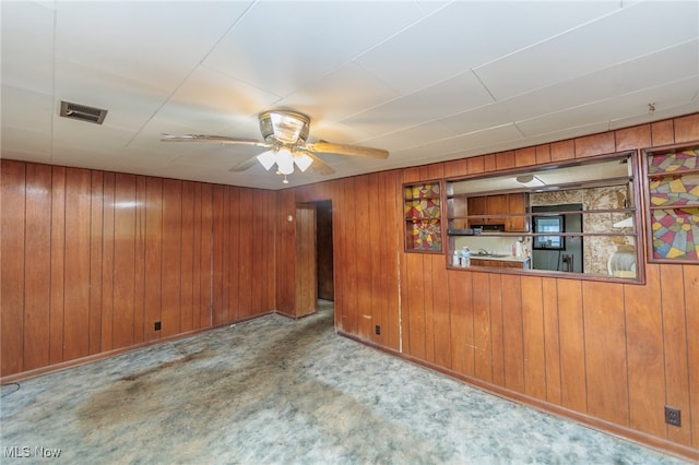 carpeted empty room with ceiling fan and wooden walls