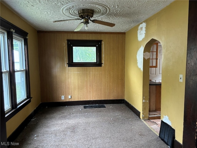 unfurnished room with wooden walls, ceiling fan, and a textured ceiling