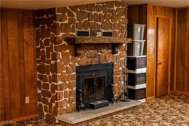 interior details with carpet flooring, a stone fireplace, wooden walls, and a textured ceiling