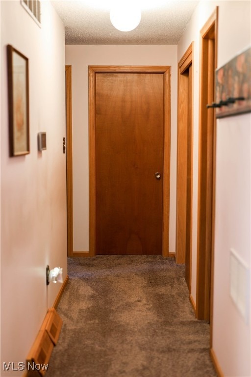 hallway featuring a textured ceiling and dark carpet