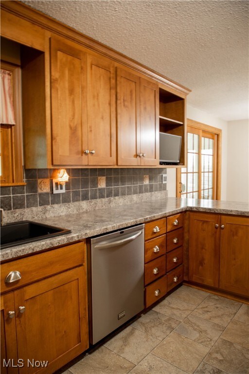 kitchen with backsplash, dishwasher, sink, and a textured ceiling