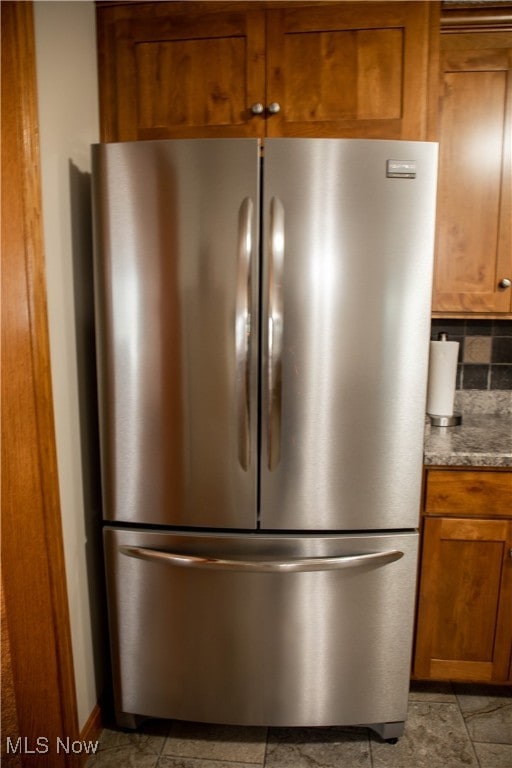 interior details featuring light stone countertops, stainless steel fridge, and backsplash