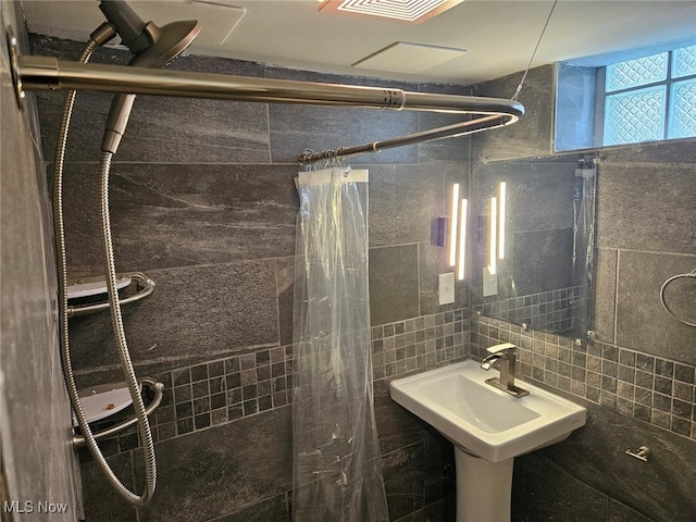 bathroom with walk in shower, tile walls, backsplash, and sink