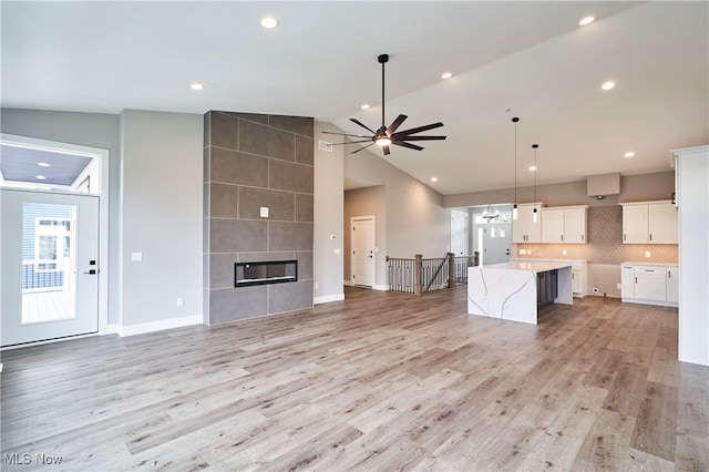 unfurnished living room with a fireplace, light wood-type flooring, high vaulted ceiling, and ceiling fan