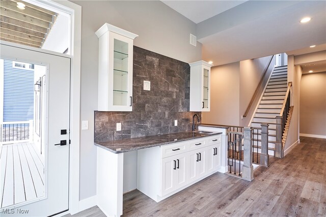 kitchen featuring backsplash, dark stone counters, sink, light wood-type flooring, and white cabinetry