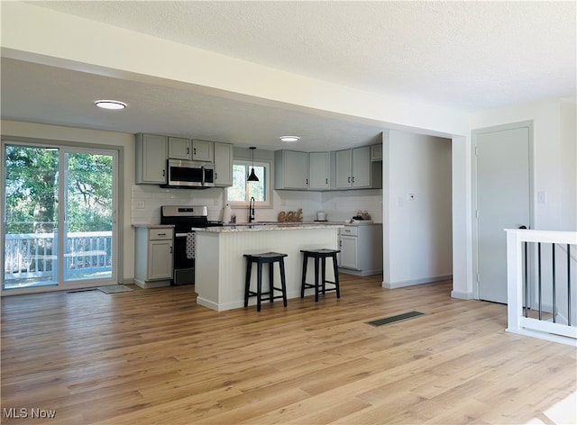 kitchen featuring appliances with stainless steel finishes, a kitchen breakfast bar, light hardwood / wood-style floors, a kitchen island, and gray cabinets