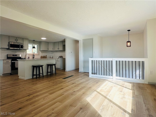 interior space with gray cabinetry, stainless steel appliances, a kitchen bar, a center island, and light hardwood / wood-style flooring