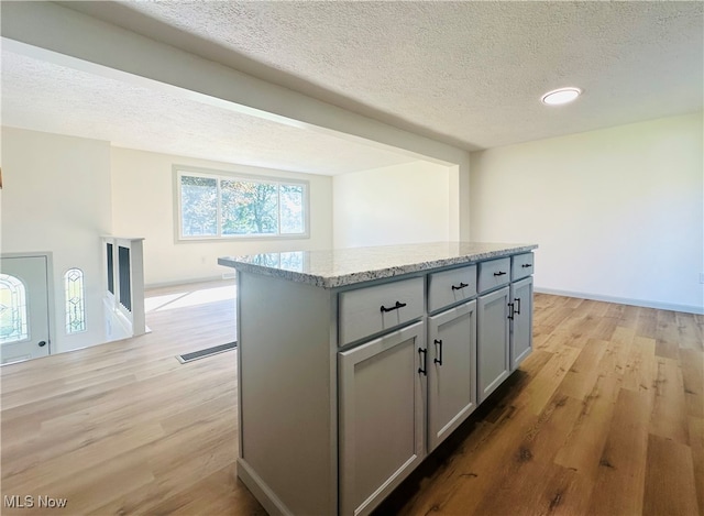 kitchen with light hardwood / wood-style floors, a kitchen island, light stone countertops, gray cabinets, and a textured ceiling