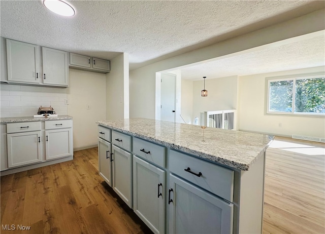 kitchen featuring light hardwood / wood-style floors, hanging light fixtures, a kitchen island, gray cabinetry, and light stone countertops