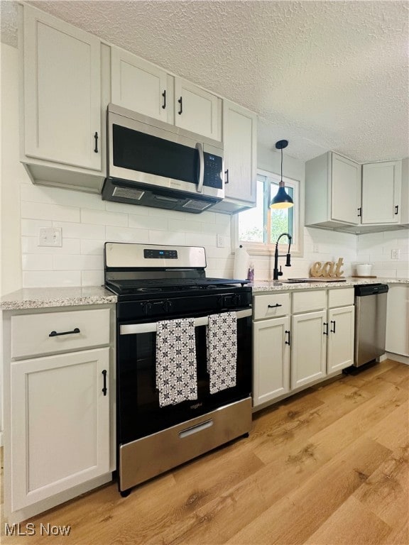 kitchen with pendant lighting, light wood-type flooring, a textured ceiling, white cabinets, and appliances with stainless steel finishes