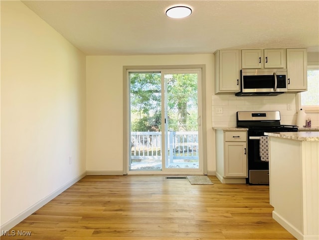 kitchen with light hardwood / wood-style flooring, appliances with stainless steel finishes, backsplash, and a healthy amount of sunlight