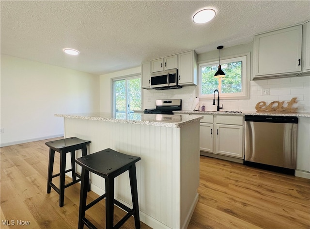 kitchen with pendant lighting, sink, plenty of natural light, appliances with stainless steel finishes, and light wood-type flooring