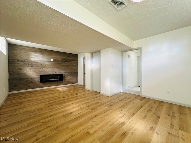 unfurnished living room featuring a textured ceiling, light hardwood / wood-style floors, and wooden walls