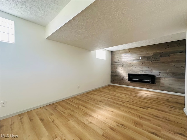 unfurnished living room featuring wooden walls, light hardwood / wood-style floors, a large fireplace, and a textured ceiling