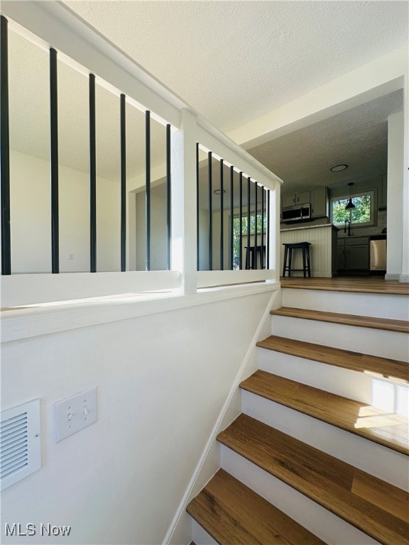 stairs featuring a textured ceiling and sink