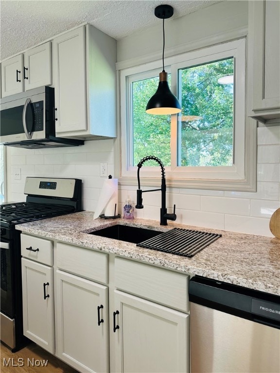 kitchen with tasteful backsplash, sink, white cabinets, hanging light fixtures, and appliances with stainless steel finishes