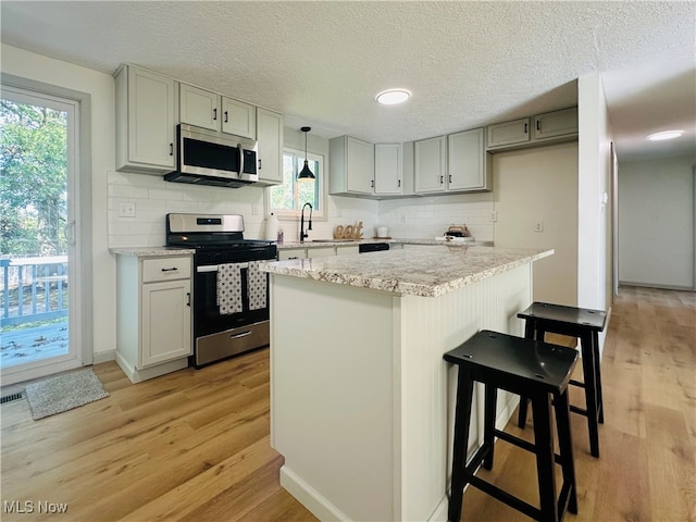 kitchen featuring stainless steel appliances, a wealth of natural light, hanging light fixtures, and light wood-type flooring