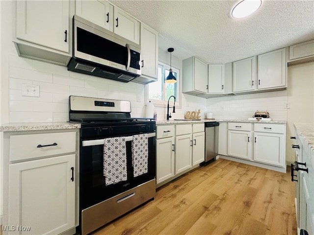 kitchen with light stone counters, sink, decorative light fixtures, light hardwood / wood-style flooring, and appliances with stainless steel finishes