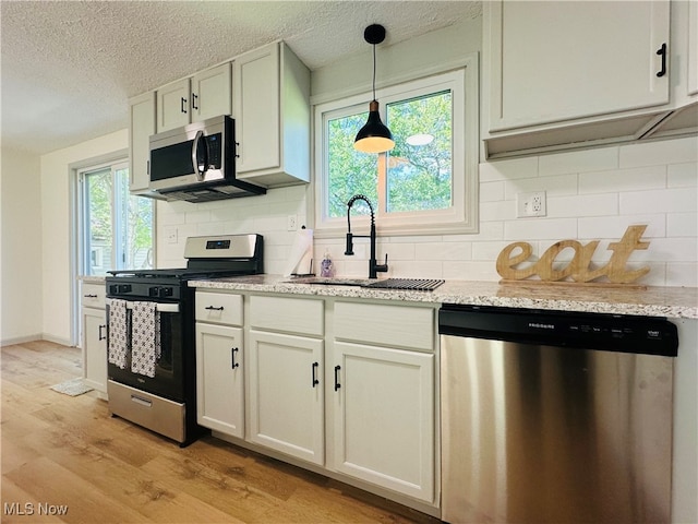 kitchen with appliances with stainless steel finishes, white cabinetry, tasteful backsplash, light hardwood / wood-style flooring, and sink