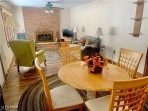 dining space with a brick fireplace, hardwood / wood-style flooring, and ceiling fan