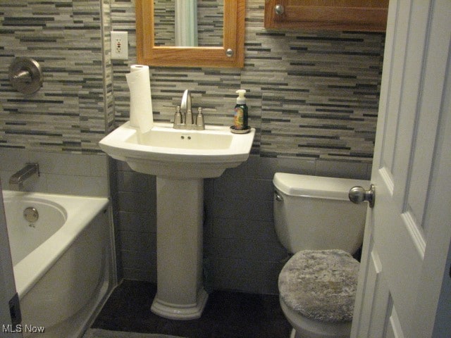 bathroom featuring tile walls, backsplash, a bathing tub, and toilet