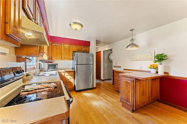 kitchen with kitchen peninsula, appliances with stainless steel finishes, sink, pendant lighting, and light hardwood / wood-style flooring