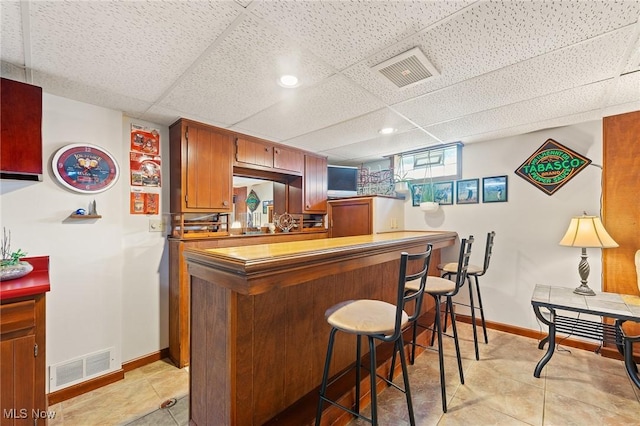 kitchen with a kitchen bar, kitchen peninsula, a paneled ceiling, and light tile patterned floors