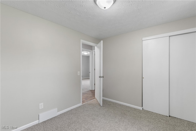 unfurnished bedroom featuring a textured ceiling, light colored carpet, and a closet