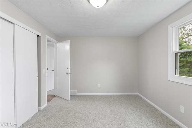 unfurnished bedroom featuring a textured ceiling, light carpet, and a closet