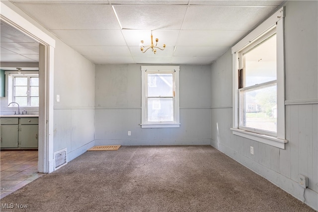 carpeted empty room with a wealth of natural light, sink, a paneled ceiling, and an inviting chandelier