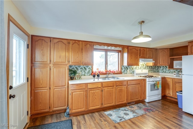 kitchen featuring white appliances, sink, hanging light fixtures, decorative backsplash, and wood-type flooring