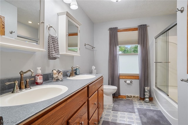 full bathroom featuring a textured ceiling, shower / bath combination with glass door, vanity, and toilet